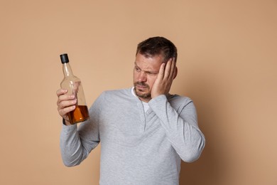 Photo of Man with bottle of whiskey suffering from hangover on beige background
