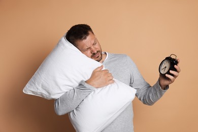 Photo of Man with pillow and alarm clock suffering from hangover on beige background