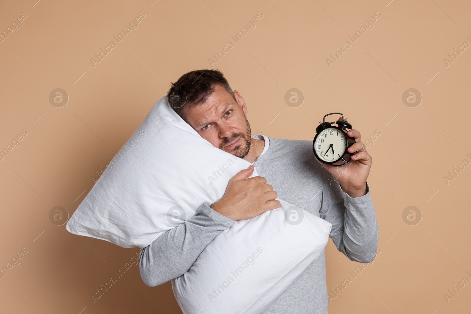 Man with pillow and alarm clock suffering from hangover on beige background Photo of Man with pillow and alarm clock suffering from hangover on beige background