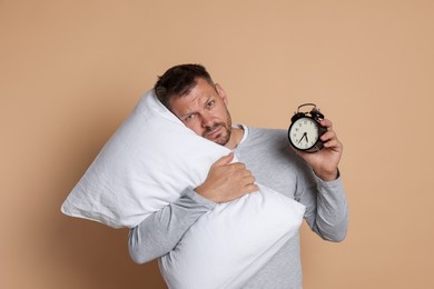 Photo of Man with pillow and alarm clock suffering from hangover on beige background