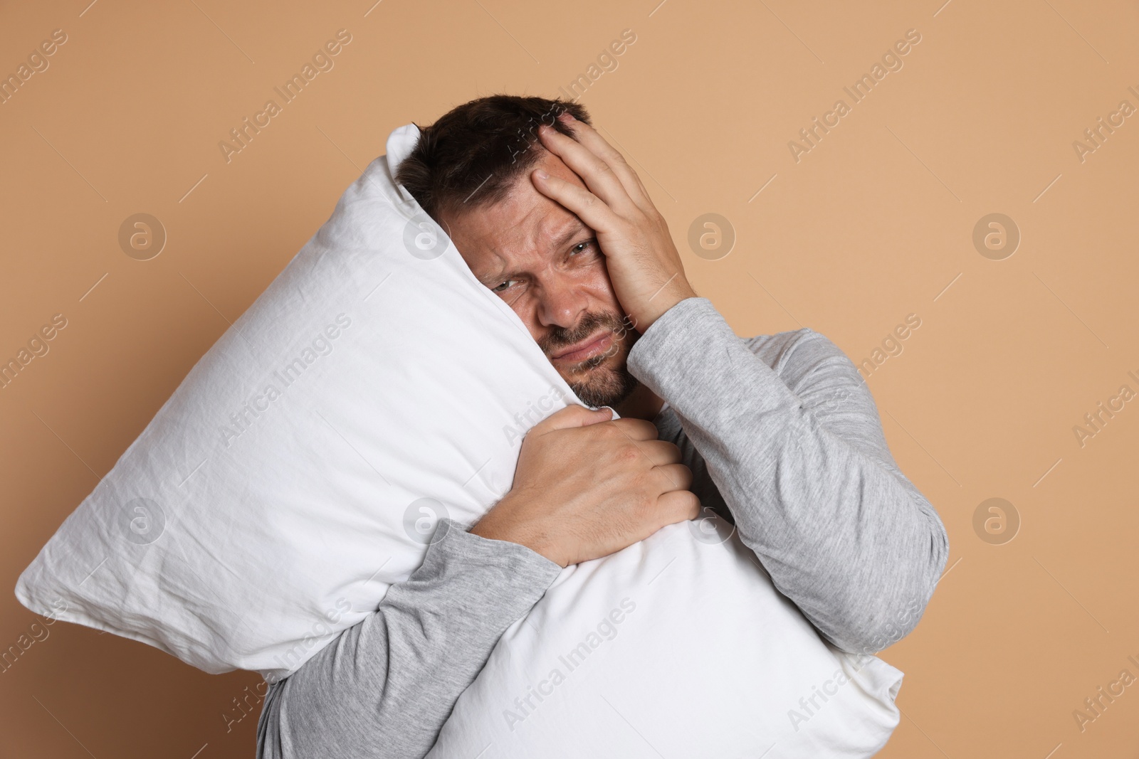 Photo of Man with pillow suffering from hangover on beige background