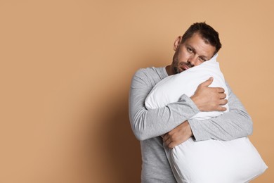 Photo of Man with pillow suffering from hangover on beige background, space for text