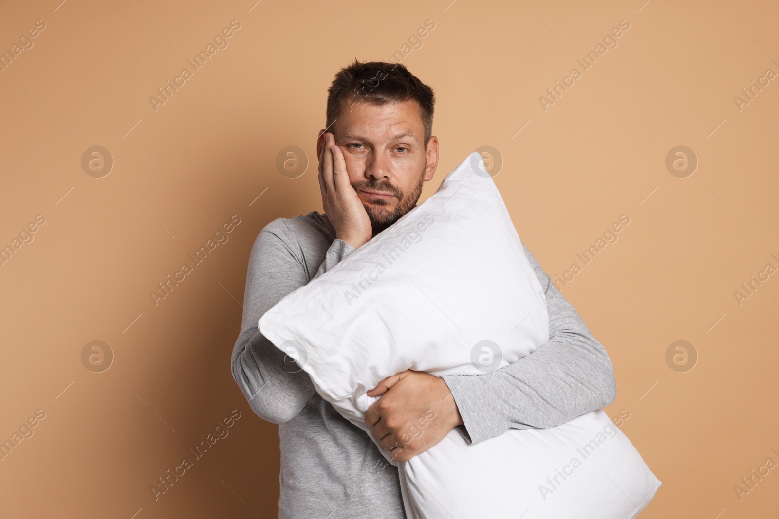Photo of Man with pillow suffering from hangover on beige background