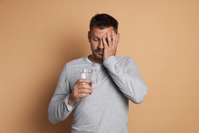 Photo of Man with glass of water suffering from hangover on beige background
