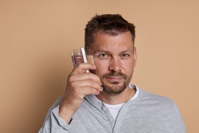 Photo of Man with glass of water suffering from hangover on beige background