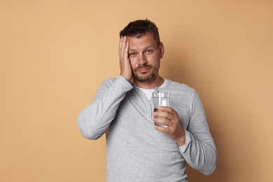 Photo of Man with glass of water suffering from hangover on beige background