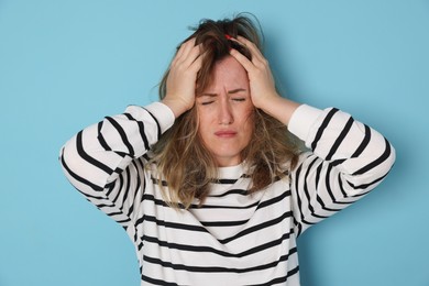 Photo of Woman suffering from hangover on light blue background