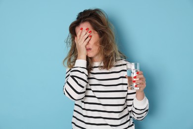 Photo of Woman with glass of water suffering from hangover on light blue background