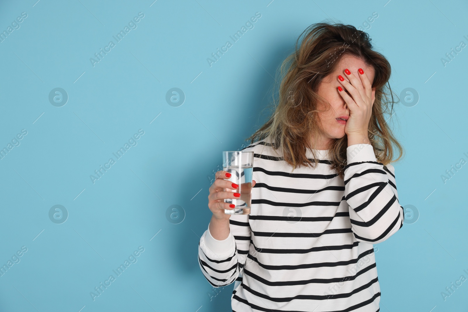 Photo of Woman with glass of water suffering from hangover on light blue background. Space for text