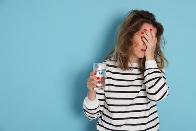 Photo of Woman with glass of water suffering from hangover on light blue background. Space for text