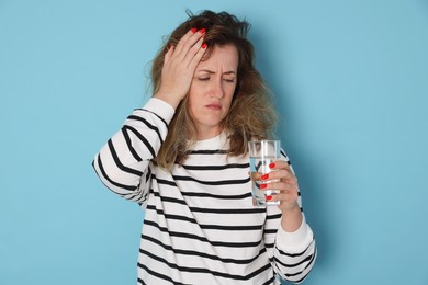 Photo of Woman with glass of water suffering from hangover on light blue background