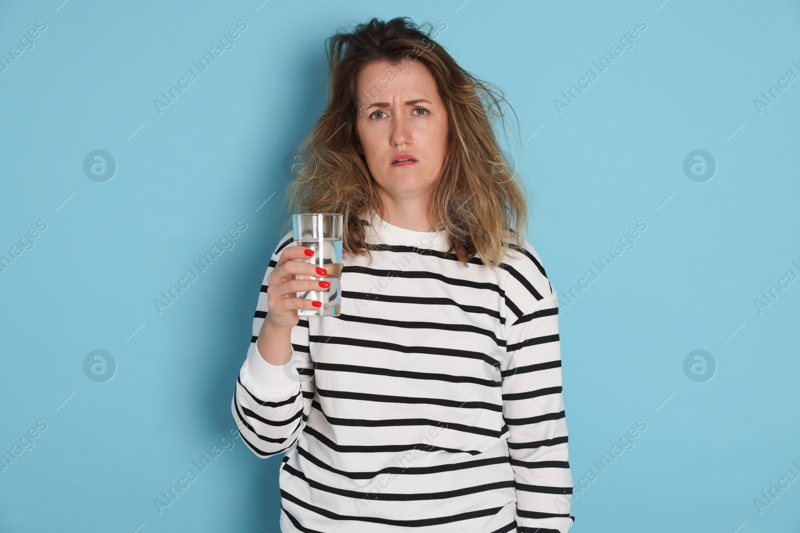 Photo of Woman with glass of water suffering from hangover on light blue background