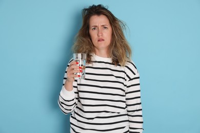 Photo of Woman with glass of water suffering from hangover on light blue background