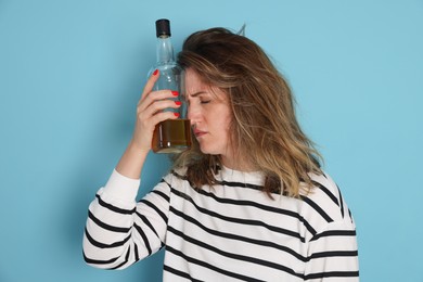 Photo of Woman with bottle of alcoholic drink suffering from hangover on light blue background