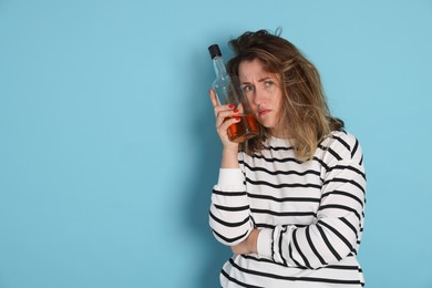 Photo of Woman with bottle of alcoholic drink suffering from hangover on light blue background. Space for text