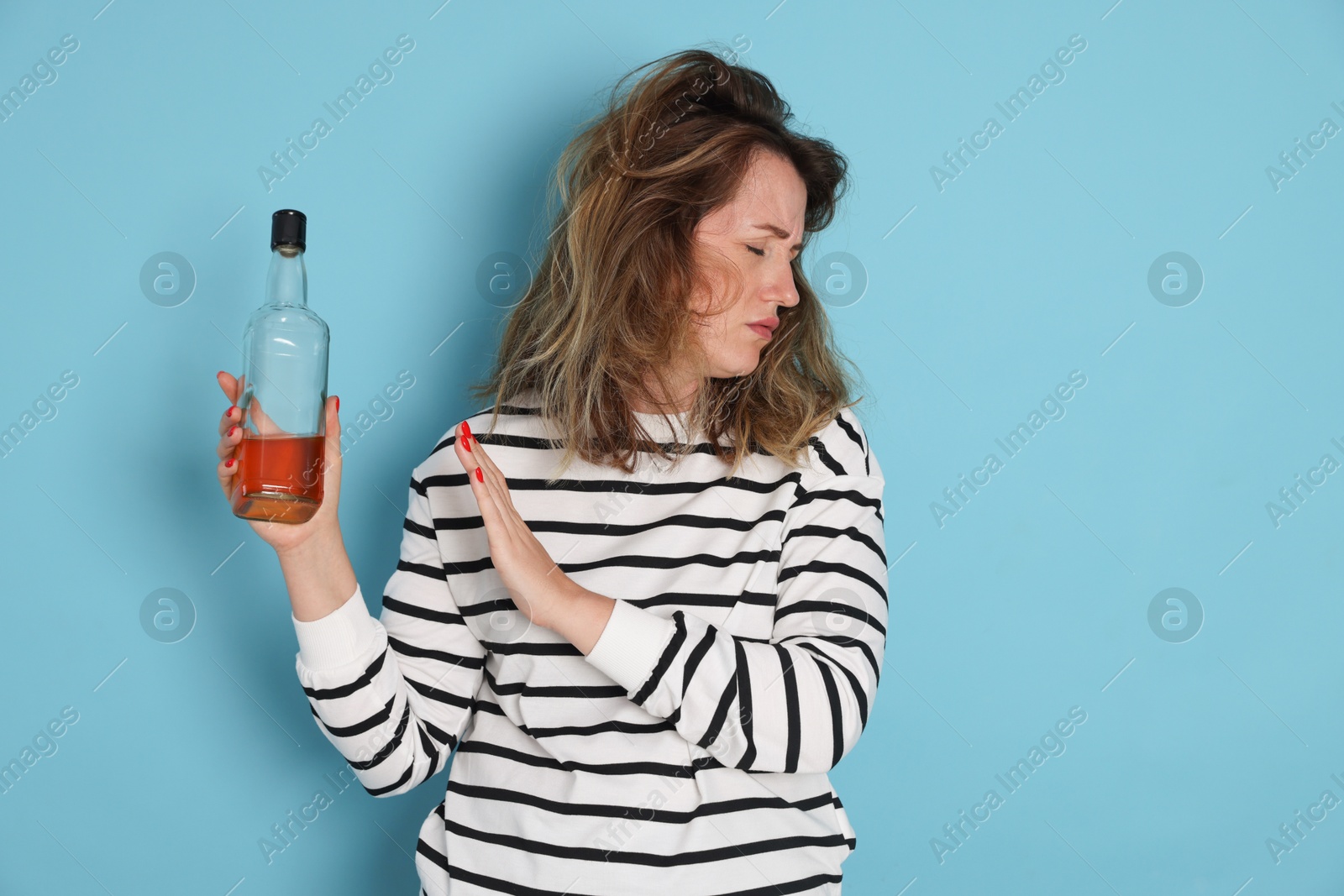Photo of Woman with bottle of alcoholic drink suffering from hangover on light blue background