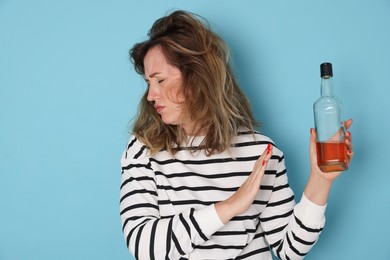 Photo of Woman with bottle of alcoholic drink suffering from hangover on light blue background
