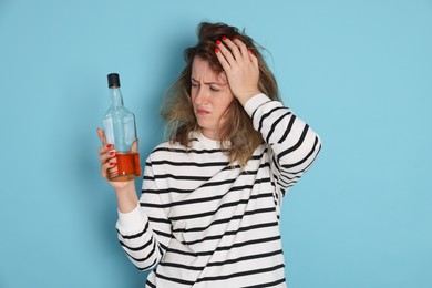 Photo of Woman with bottle of alcoholic drink suffering from hangover on light blue background