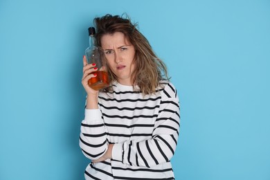 Photo of Woman with bottle of alcoholic drink suffering from hangover on light blue background