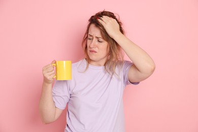 Photo of Woman with cup of coffee suffering from hangover on pink background