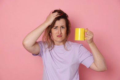 Photo of Woman with cup of coffee suffering from hangover on pink background