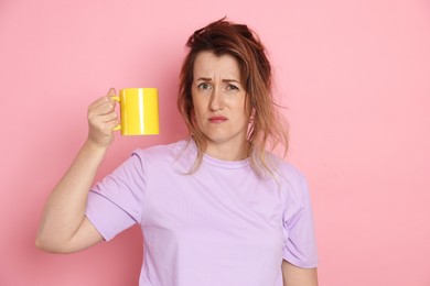 Photo of Woman with cup of coffee suffering from hangover on pink background