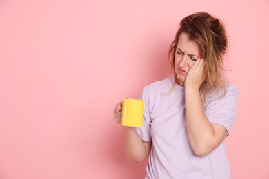 Photo of Woman with cup of coffee suffering from hangover on pink background. Space for text