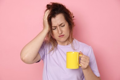Photo of Woman with cup of coffee suffering from hangover on pink background