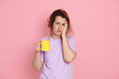 Photo of Woman with cup of coffee suffering from hangover on pink background