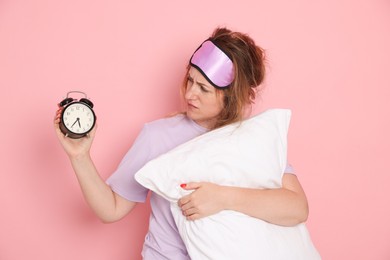 Photo of Woman with pillow and alarm clock suffering from hangover on pink background