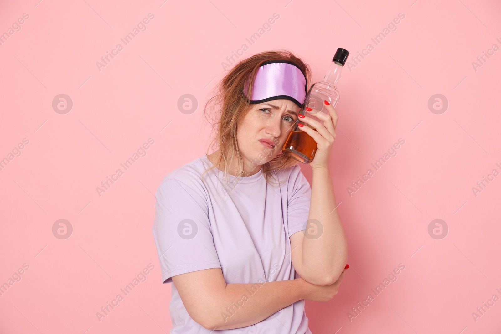 Woman with bottle of alcoholic drink suffering from hangover on pink background Photo of Woman with bottle of alcoholic drink suffering from hangover on pink background