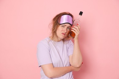 Photo of Woman with bottle of alcoholic drink suffering from hangover on pink background