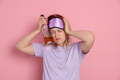 Photo of Woman with bottle of alcoholic drink suffering from hangover on pink background