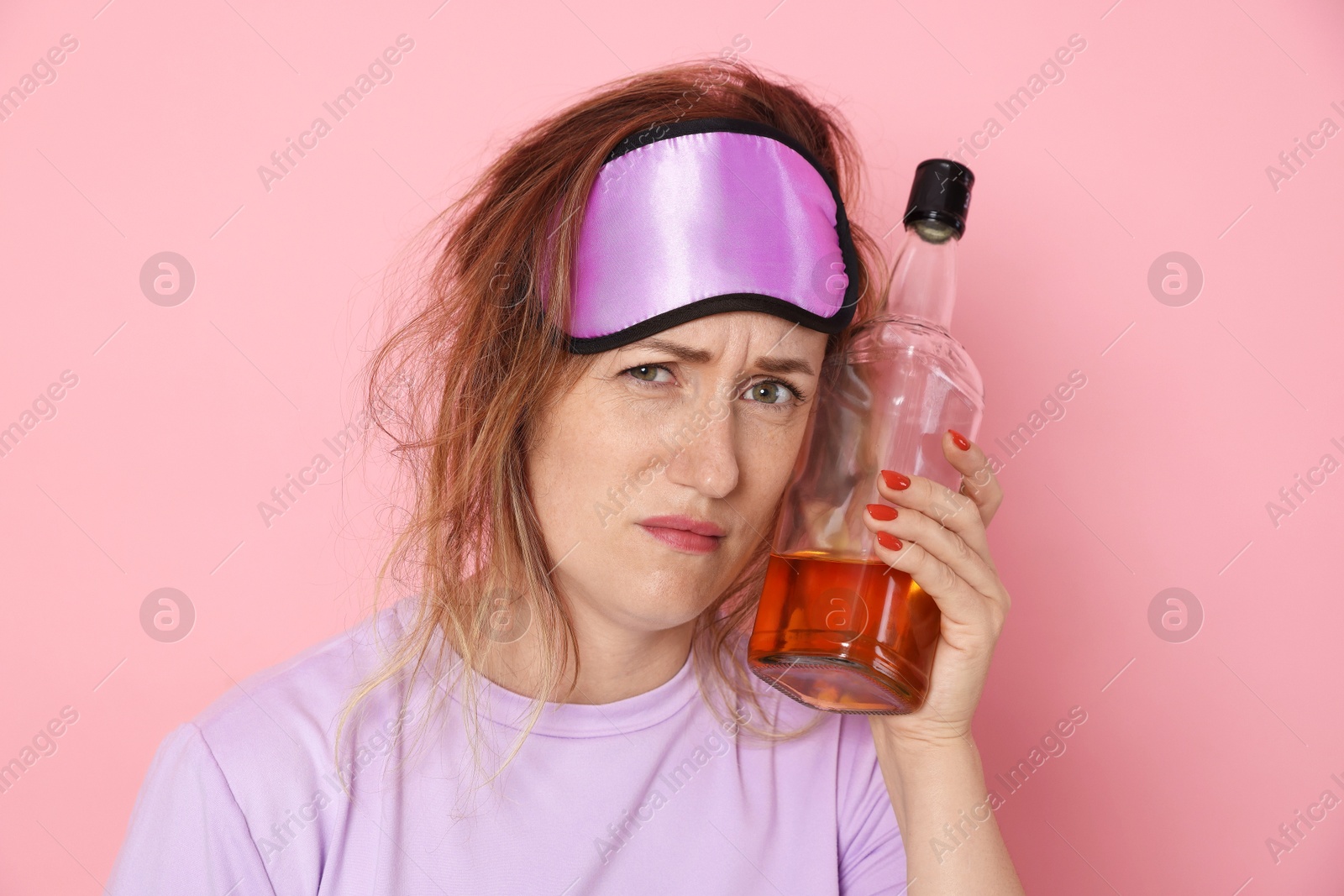 Woman with bottle of alcoholic drink suffering from hangover on pink background Photo of Woman with bottle of alcoholic drink suffering from hangover on pink background
