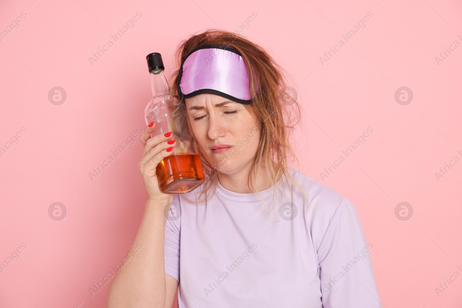 Photo of Woman with bottle of alcoholic drink suffering from hangover on pink background