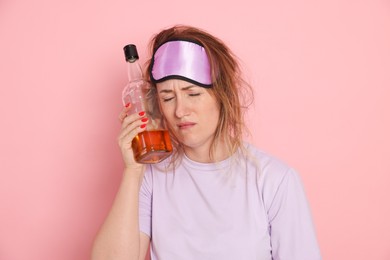 Photo of Woman with bottle of alcoholic drink suffering from hangover on pink background