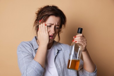 Photo of Woman with bottle of alcoholic drink suffering from hangover on beige background