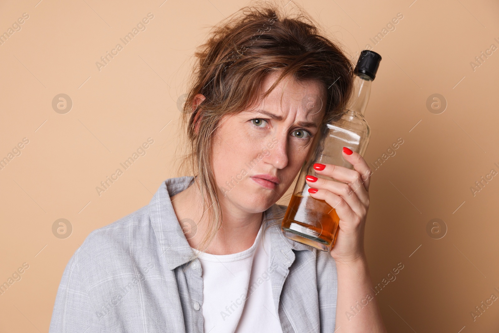 Photo of Woman with bottle of alcoholic drink suffering from hangover on beige background