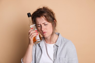 Photo of Woman with bottle of alcoholic drink suffering from hangover on beige background