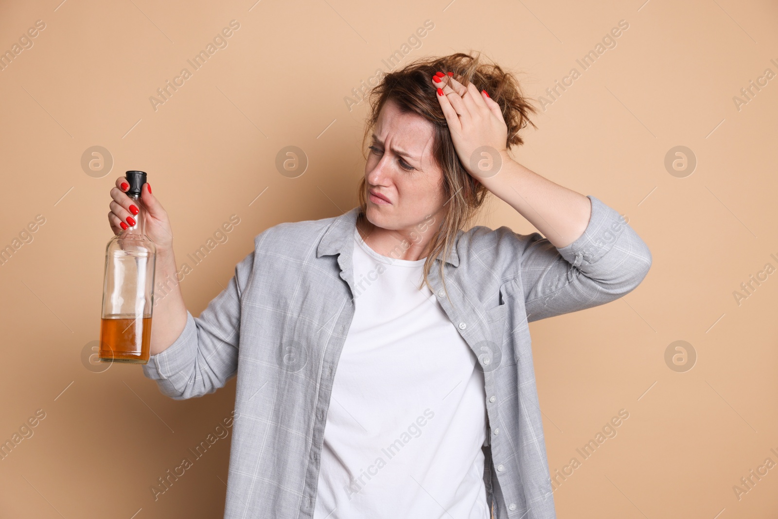 Woman with bottle of alcoholic drink suffering from hangover on beige background Photo of Woman with bottle of alcoholic drink suffering from hangover on beige background