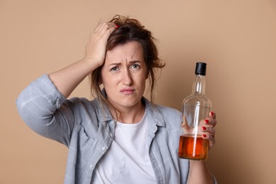 Photo of Woman with bottle of alcoholic drink suffering from hangover on beige background