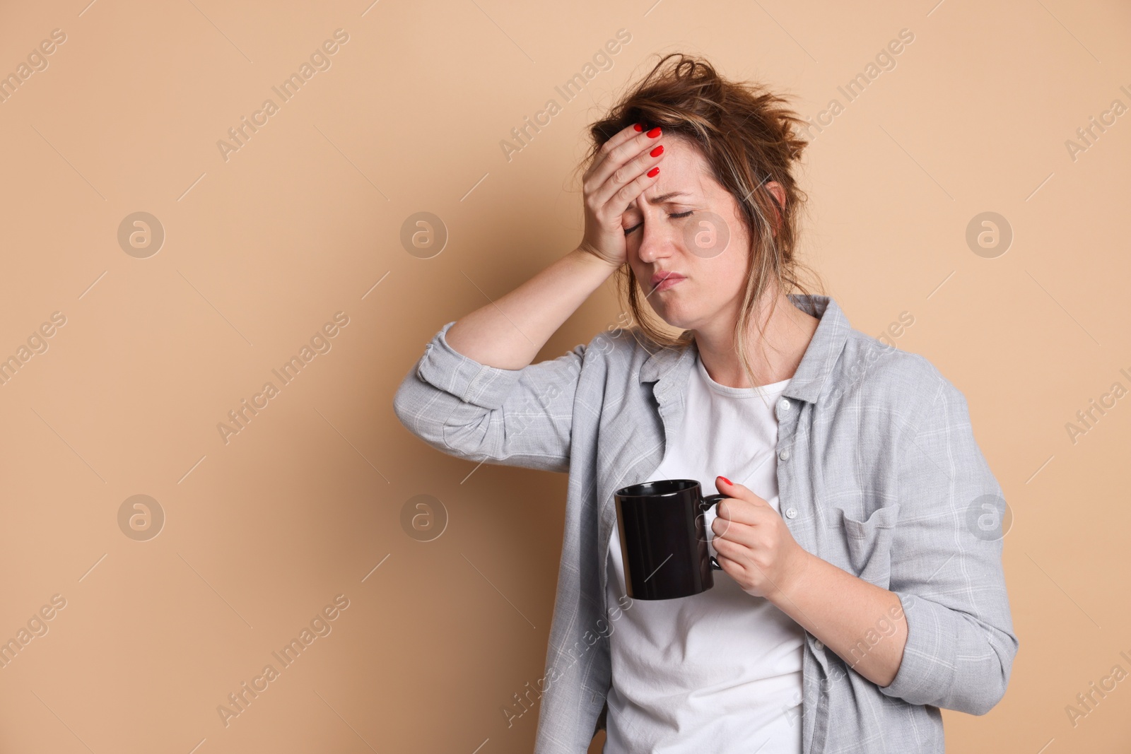 Photo of Woman with cup of coffee suffering from hangover on beige background. Space for text