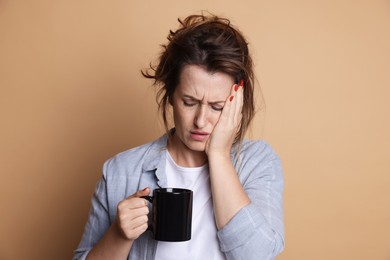 Photo of Woman with cup of coffee suffering from hangover on beige background