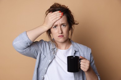Photo of Woman with cup of coffee suffering from hangover on beige background