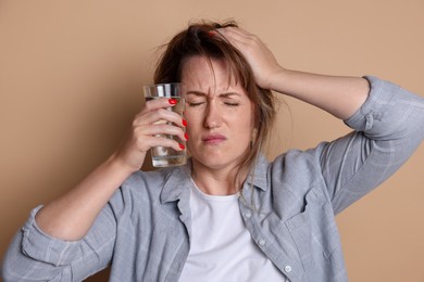 Photo of Woman with glass of water suffering from hangover on beige background
