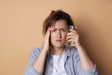 Photo of Woman with glass of water suffering from hangover on beige background