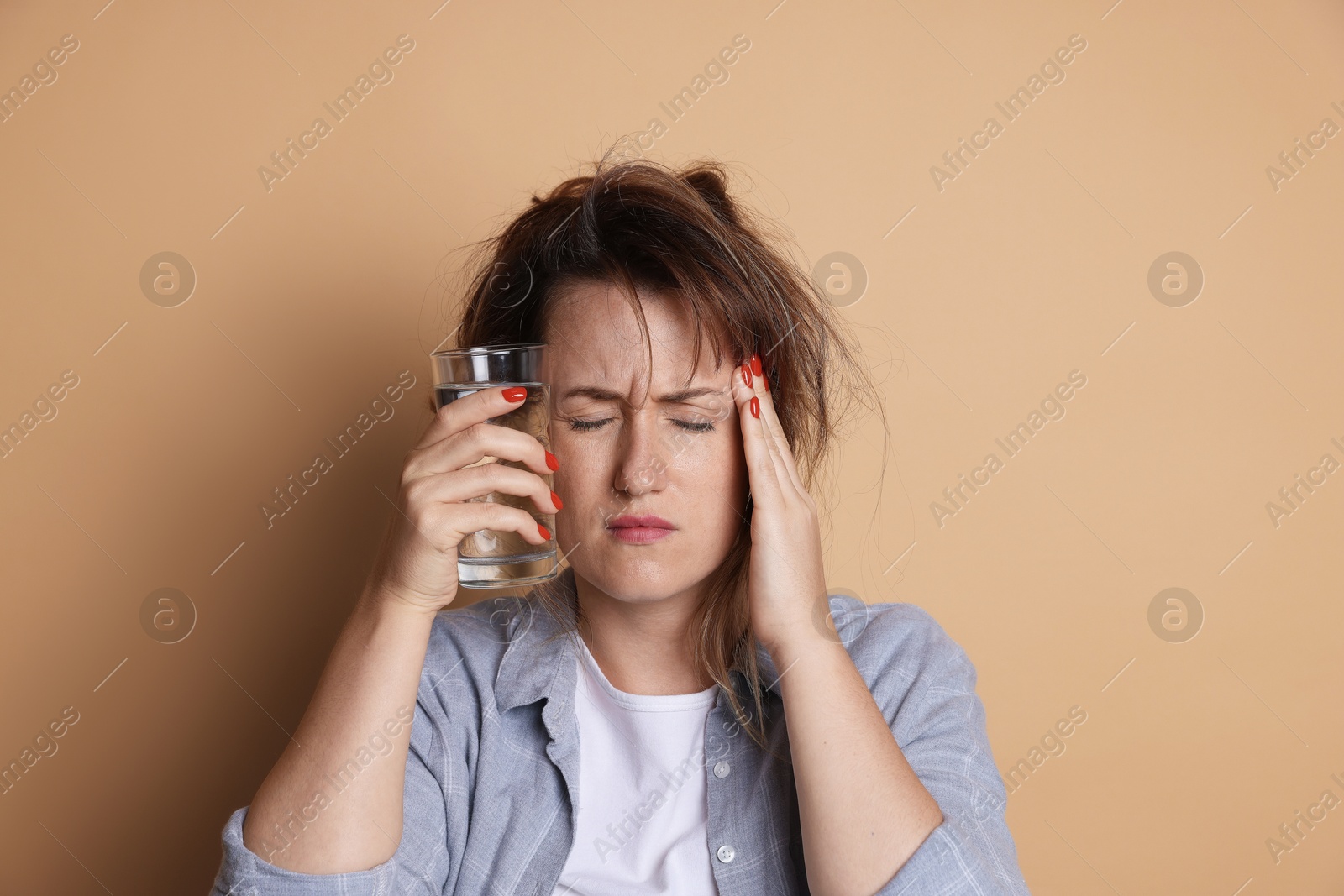 Photo of Woman with glass of water suffering from hangover on beige background