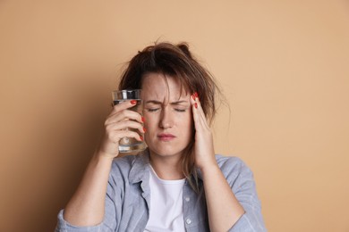 Photo of Woman with glass of water suffering from hangover on beige background