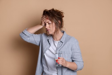 Photo of Woman with glass of water suffering from hangover on beige background