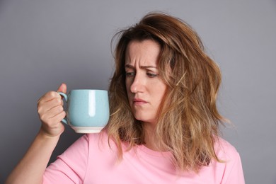 Photo of Woman with cup of coffee suffering from hangover on grey background